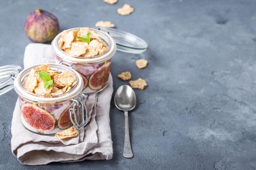 Homemade healthy yoghurt in glass pot with cereals, figs, mint on rustic stone background. Space for text. Healthy morning breakfast. Freshly made yoghurt, oat granola and fruit. Healthy eating