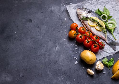 Raw fish with fresh ingredients ready to cook. Fish, lemon, herbs, potato, tomatoes. Ingredients for cooking on dark rustic background. Space for text. Diet and healthy food. Fish background. Top view