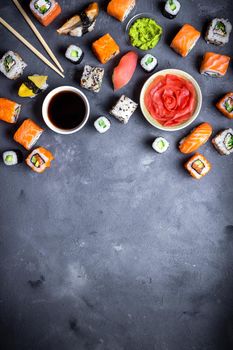 Japanese sushi on a rustic dark background. Sushi rolls, nigiri, maki, pickled ginger, wasabi, soy sauce. Sushi set on a table. Space for text. Top view. Sushi background. Asian or Japanese food frame