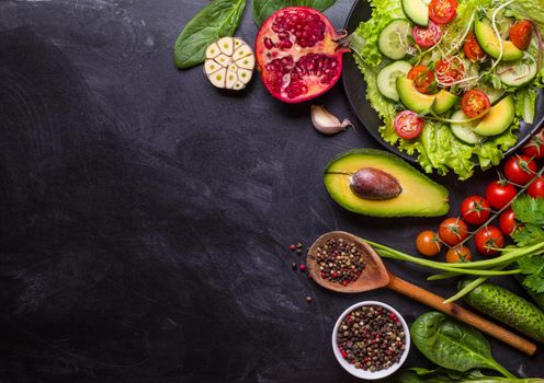 Ingredients for making salad on rustic black chalk board background. Vegetable salad in bowl, avocado, tomato, cucumber, spinach. Healthy, clean eating concept. Vegan or gluten free diet. Copy space