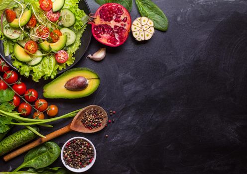 Ingredients for making salad on rustic black chalk board background. Vegetable salad in bowl, avocado, tomato, cucumber, spinach. Healthy, clean eating concept. Vegan or gluten free diet. Copy space