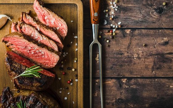 Sliced grilled marbled meat steak Filet Mignon, seasonings, fork, wooden cutting board. Space for text. Juicy meat steak. Beef steak grilled/fried. Top view. Roasted meat steak. Close-up. Rustic