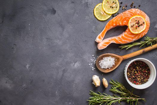 Fresh raw salmon steak, lemon, herbs, spices, wooden spoon on dark rustic concrete background. Food frame. Ingredients set for making healthy dinner. Healthy/diet concept. Space for text. Fresh fish