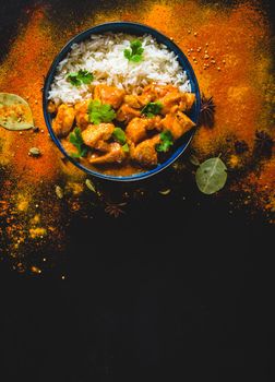 Indian Butter chicken with basmati rice in bowl, spices, black background. Space for text. Butter chicken, traditional Indian dish. Top view. Chicken tikka masala. Indian cuisine concept. Overhead