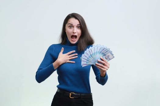 Surprised woman in a blue pullover holds a lot of tenge money in her hands.