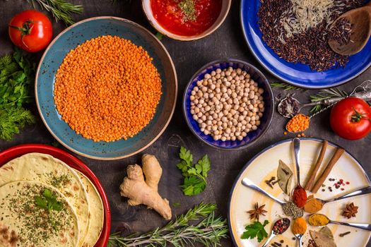 Table served with traditional for asian or eastern cuisine food. Cereal grains, beans, spices on colorful plates. Lentil, basmati and wild rice mix, chick-pea, tomato chutney, pita. Ingredients for indian or eastern food