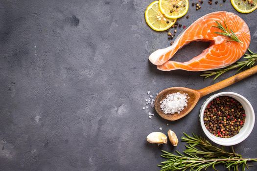Fresh raw salmon steak, lemon, herbs, spices, wooden spoon on dark rustic concrete background. Food frame. Ingredients set for making healthy dinner. Healthy/diet concept. Space for text. Fresh fish