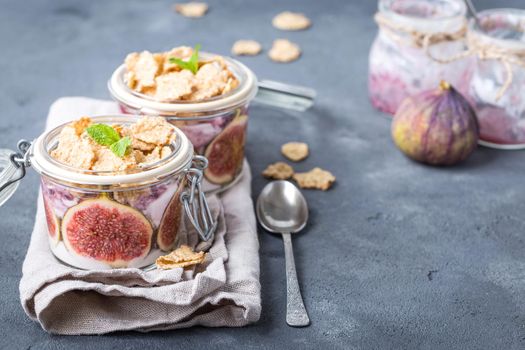 Homemade healthy yoghurt in glass pot with cereals, figs, mint on rustic stone background. Space for text. Healthy morning breakfast. Freshly made yoghurt, oat granola and fruit. Healthy eating