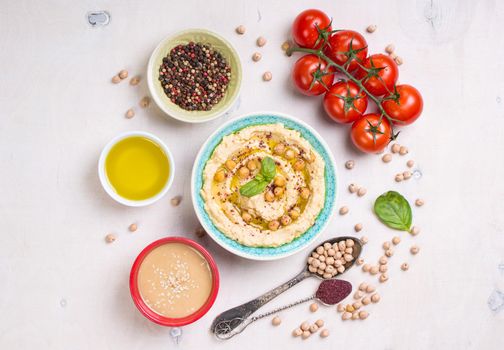 Hummus ingredients. Chickpea, tahini paste, olive oil, sesame seeds, sumac, herbs on white rustic wooden background. Set of raw ingredients for making hummus. Middle eastern cuisine. Top view