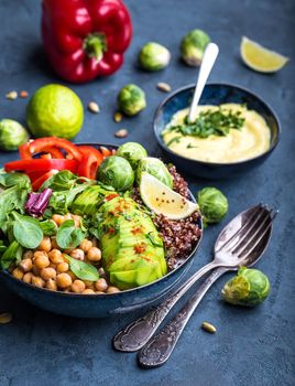 Bowl with healthy salad and dip. Close-up. Buddha bowl with chickpea, avocado, quinoa seeds, red bell pepper, fresh spinach, brussels sprout, lime mix. Vegetarian salad. Clean healthy eating concept