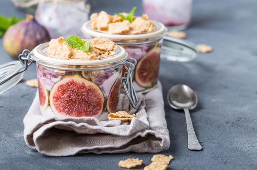 Homemade healthy yoghurt in glass pot with cereals, figs, mint on rustic concrete background. Healthy morning breakfast. Freshly made yoghurt with oat granola and fruit. Yoghurt in jar with muesli