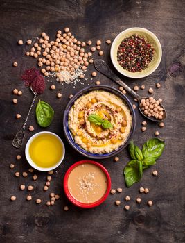 Hummus ingredients. Chickpea, tahini paste, olive oil, sesame seeds, sumac, herbs on dark rustic wooden background. Set of raw ingredients for making hummus. Middle eastern cuisine. Top view