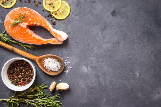 Fresh raw salmon steak, lemon, herbs, spices, wooden spoon on dark rustic concrete background. Food frame. Ingredients set for making healthy dinner. Healthy/diet concept. Space for text. Fresh fish