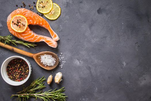 Fresh raw salmon steak, lemon, herbs, spices, wooden spoon on dark rustic concrete background. Food frame. Ingredients set for making healthy dinner. Healthy/diet concept. Space for text. Fresh fish