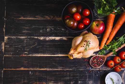 Raw whole chicken ready for cooking. Chicken with vegetables, herbs and spices on a black rustic wooden background. Space for text. Food frame. Diet or healthy eating. Ingredientd for cooking