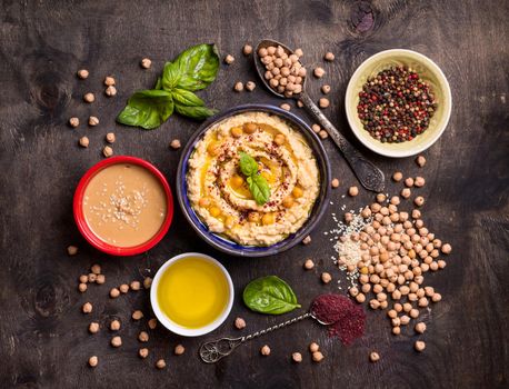 Hummus ingredients. Chickpea, tahini paste, olive oil, sesame seeds, sumac, herbs on dark rustic wooden background. Set of raw ingredients for making hummus. Middle eastern cuisine. Top view