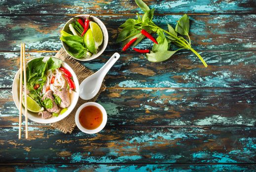 Traditional Vietnamese soup Pho bo with herbs, meat, rice noodles, broth. Pho bo in bowl with chopsticks, spoon. Space for text. Top view. Asian soup Pho bo on wooden table background. Vietnamese soup