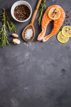 Fresh raw salmon steak, lemon, herbs, spices, wooden spoon on dark rustic concrete background. Food frame. Ingredients set for making healthy dinner. Healthy/diet concept. Space for text. Fresh fish