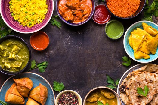 Assorted indian food on dark wooden background. Dishes of indian cuisine. Curry, butter chicken, rice, lentils, paneer, samosa, naan, chutney, spices. Space for text. Bowls and plates with indian food