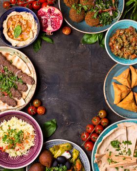 Middle eastern or arabic dishes and assorted meze on a dark background. Meat kebab, falafel, baba ghanoush, hummus, rice with vegetables, sambusak, kibbeh, pita. Halal food. Space for text. Top view