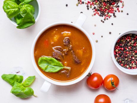 Delicious tomato soup with meat on a white rustic wooden table with fresh cherry tomatoes, basil leaves and dry pepper. Ingredients for soup. Top view