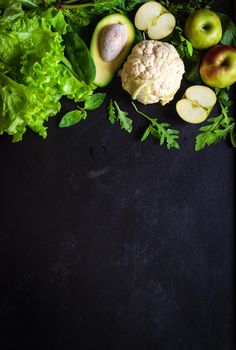 Fresh green vegetables and fruits on black chalk board background. Сauliflower, avocado, spinach, lettuce salad, green apples, herbs. Vegetarian food. Diet/healthy/detox food concept. Space for text