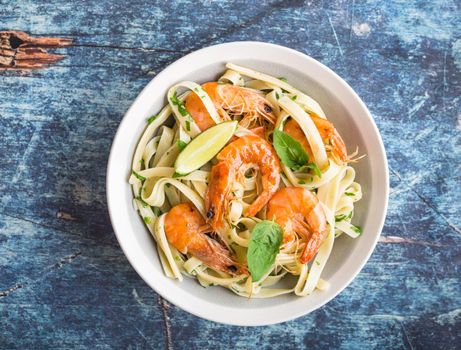 Homemade pasta with fried shrimps and basil on rustic wooden blue background. Pasta with seafood in plate. Top view. Close-up. Mediterranean cuisine. Pasta for dinner or lunch. Linguine with prawns