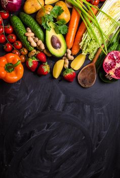 Vegetables, fruits, herbs, raw ingredients for cooking and spoon on rustic black chalk board background. Healthy, clean eating concept. Vegan or gluten free diet. Space for text. Top view. Food frame