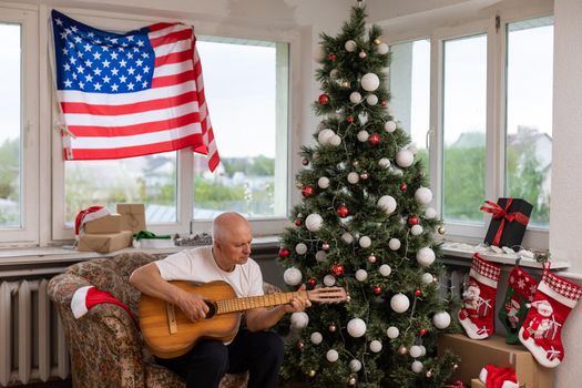 Man playing acoustic guitar, American flag, at christmas.