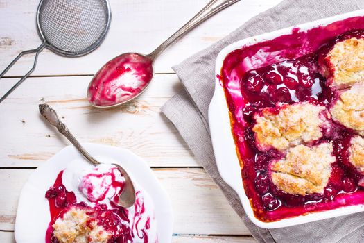 Homemade cherry cobbler pie with flaky crust, ice cream, vintage spoon, sieve for flour. Top view on the white wooden table.