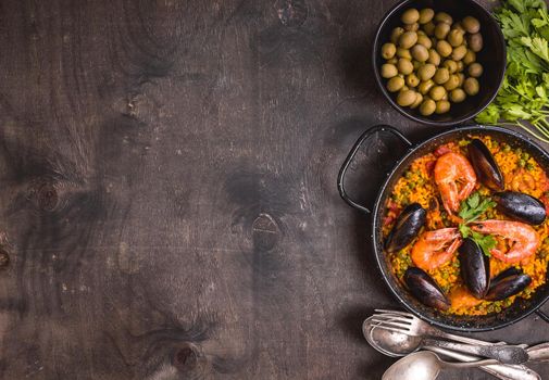 Paella background, space for text. Paella in black pan with saffron rice, peas, shrimps, mussels, squid, meat. Seafood paella, traditional spanish dish. Paella on rustic black wooden table. Top view