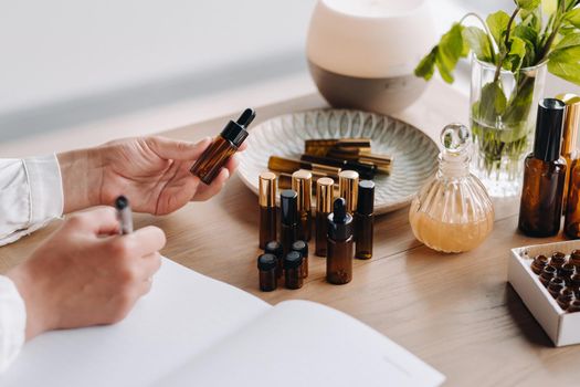 Close-up of female hands holding a bottle of essential oil and writing an entry in a notebook, aromatherapy.