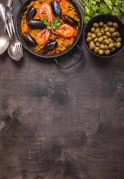 Paella background, space for text. Paella in black pan with saffron rice, peas, shrimps, mussels, squid, meat. Seafood paella, traditional spanish dish. Paella on rustic black wooden table. Top view