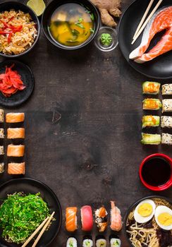 Sushi and japanese food on dark background. Sushi rolls, hiyashi wakame, miso soup, ramen, fried rice with vegetables, nigiri, salmon steak, soy sauce, сhopsticks. Asian/Japanese food frame. Overhead....