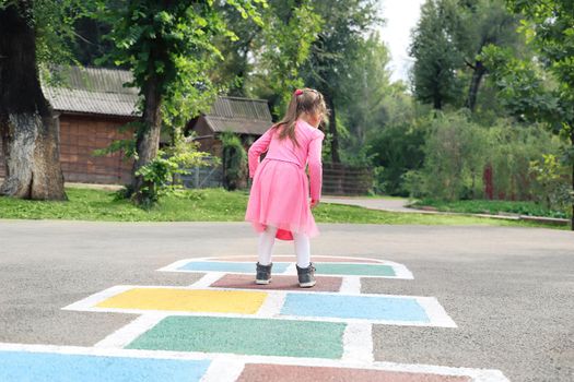 Little girl in a pink dress plays hopscotch on the street.