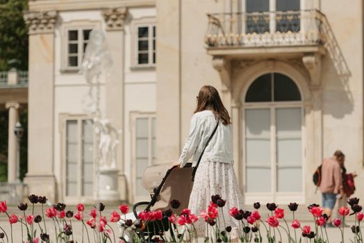 A photo from behind of the mother who is walking with her baby in the stroller on the territory of the palace.