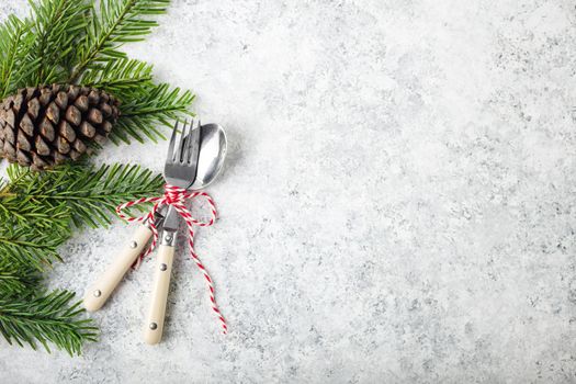 Christmas/New Year background. Christmas table place setting. Festive dinner background. Spoon, fork, fir branch on white concrete background. Christmas decoration. Space for text. Top view. Holidays