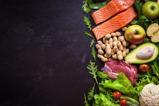 Fresh vegetables, fruits, fish, meat, nuts on black chalk board background. Сauliflower, avocado, apples, tomatoes, salmon, beef, spinach, herbs. Diet/healthy/paleo food. Ingredients. Space for text