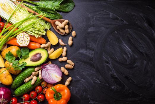 Vegetables, herbs, nuts, ingredients for cooking, wooden spoon on rustic black chalk board background. Healthy, clean eating concept. Vegan or gluten free diet. Space for text. Top view. Salad making