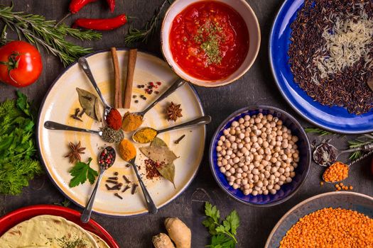 Assorted spices, herbs, chick-pea, lentil, basmati and wild rice mix, tomato chutney and pita on colorful plates. Top view. Spices and different food. Indian/ayurvedic food...