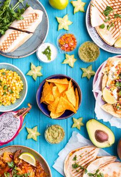 Assorted mix of traditional Mexican food. Different Mexican dishes table. Cheese nachos, tacos, guacamole, quesadilla, burrito, fajitas, tortilla chips, Mexican fruits. Tex-Mex cuisine. Mexico style