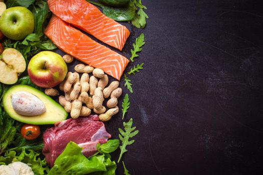 Fresh vegetables, fruits, fish, meat, nuts on black chalk board background. Сauliflower, avocado, apples, tomatoes, salmon, beef, spinach, herbs. Diet/healthy/paleo food. Ingredients. Space for text