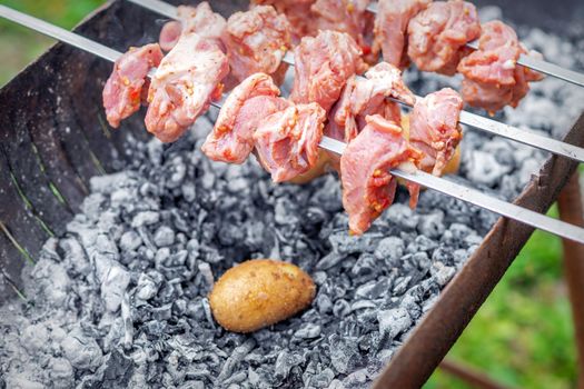 Hands of man prepares barbecue meat with potatoes on skewer by grill on fire outdoors. Concept of lifestyle rustic food preparation