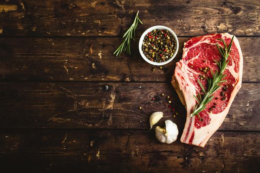 Raw marbled meat steak, pepper, herbs, garlic, old wooden background. Space for text. Beef Rib eye steak ready for cooking. Top view. Copy space. Ingredients, meat roasting. Ribeye meat steak. Closeup