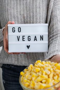 Lightbox with text GO VEGAN in female hands. Veganism, vegetarian healthy lifestyle. Frozen food in bowl. Healthy eating vegan. Yellow corn