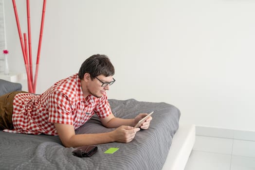 Online shopping concept. Young man lying on the bed and shopping online using tablet