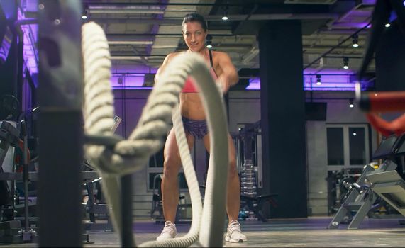Woman athlete training using battle ropes. Sportswoman's workout in gym. Slow motion