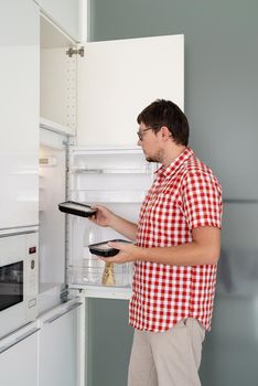 Delivery food, products to home. Shopping and healthy food concept. Young man in red plaid shirt holding disposable plastic boxed with food and putting them to the refridgerator