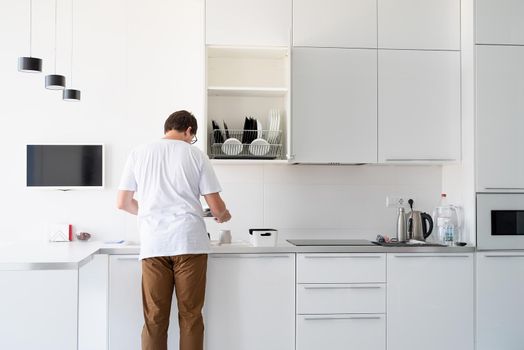 Doing chores. Man in white shirt washing dishes in the modern kitchen. Minimal modern kitchen interior