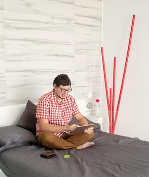 Online shopping concept. Young man sitting on the bed and shopping online using tablet